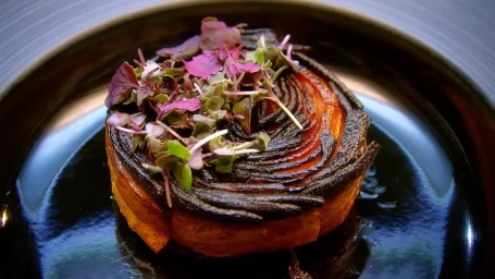 Gourmet layered vegetable tart topped with purple microgreens on a glossy dark plate by Pete Campbell