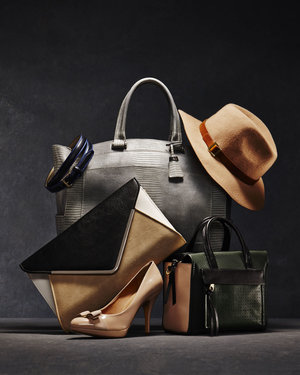 Studio shot featuring a collection of handbags, beige high heels, and a hat against a dark gray background, styled for fashion.