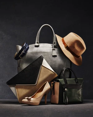 Studio shot featuring a collection of handbags, beige high heels, and a hat against a dark gray background, styled for fashion.