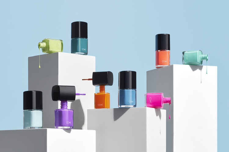 Collection of colorful nail polish bottles arranged on white cubes against a light blue backdrop, creating a vibrant beauty product display.