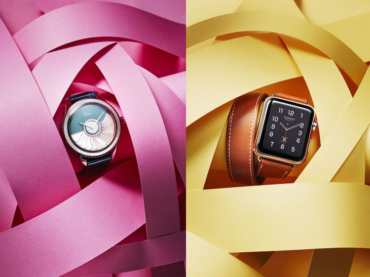 Two luxury watches, a Dior and an Hermes Apple Watch, are showcased against pink and yellow paper ribbon backgrounds, product photography.