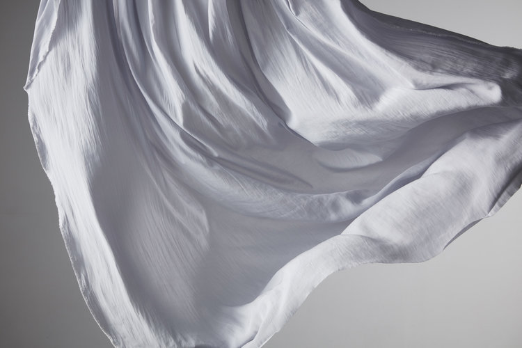 Abstract flowing white fabric. Light dances across the delicate folds of a soft, billowing material in a studio setting.