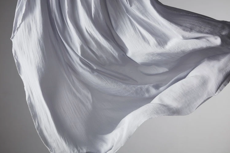Abstract flowing white fabric. Light dances across the delicate folds of a soft, billowing material in a studio setting.