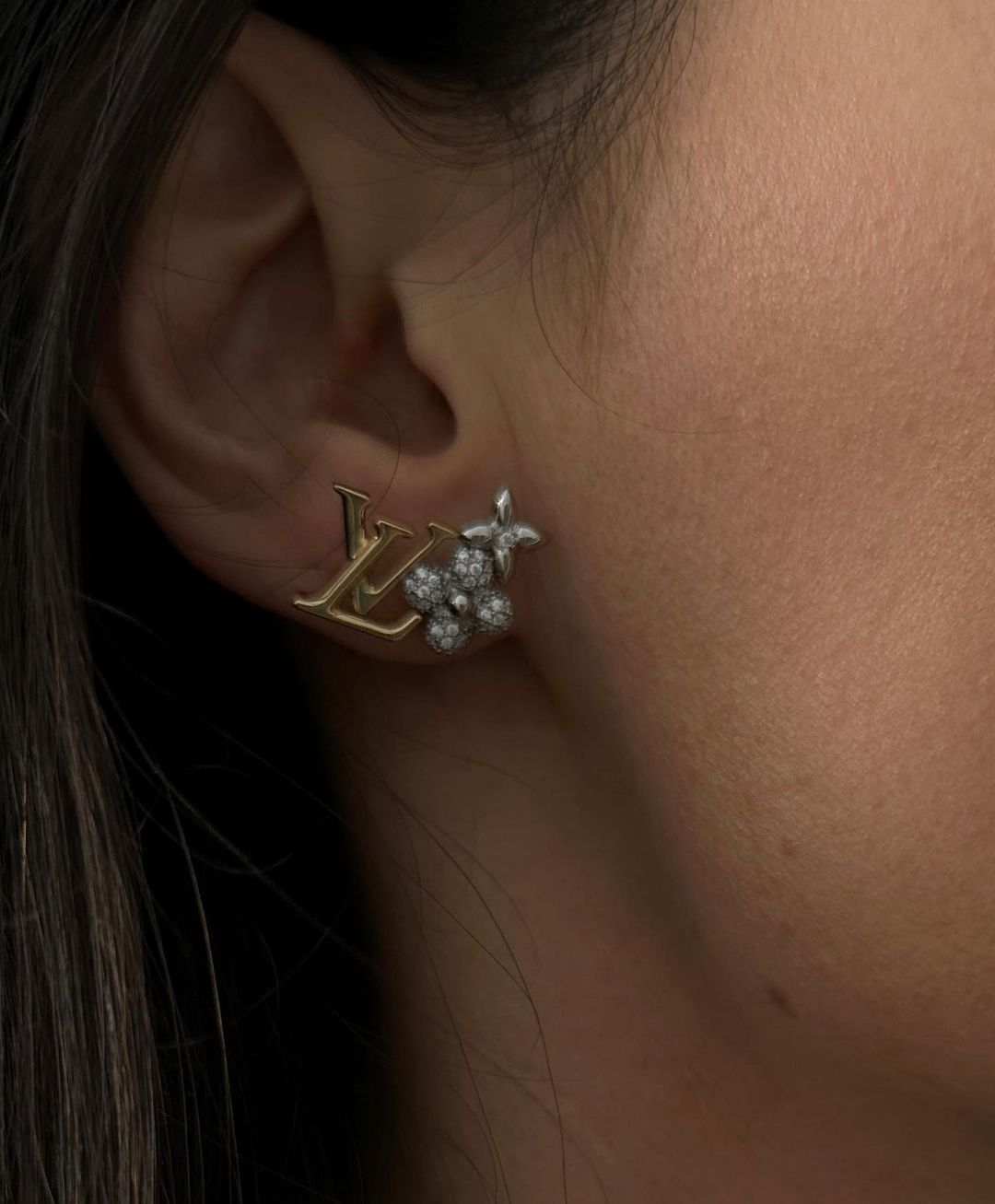 Close-up of a woman's ear wearing a Louis Vuitton earring with flower and diamond details, showcased indoors with a neutral backdrop.