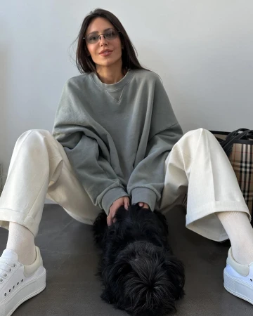 Woman in sweatshirt sitting with dog indoors with Burberry tote bag in background; casual fashion, simple background, natural light.