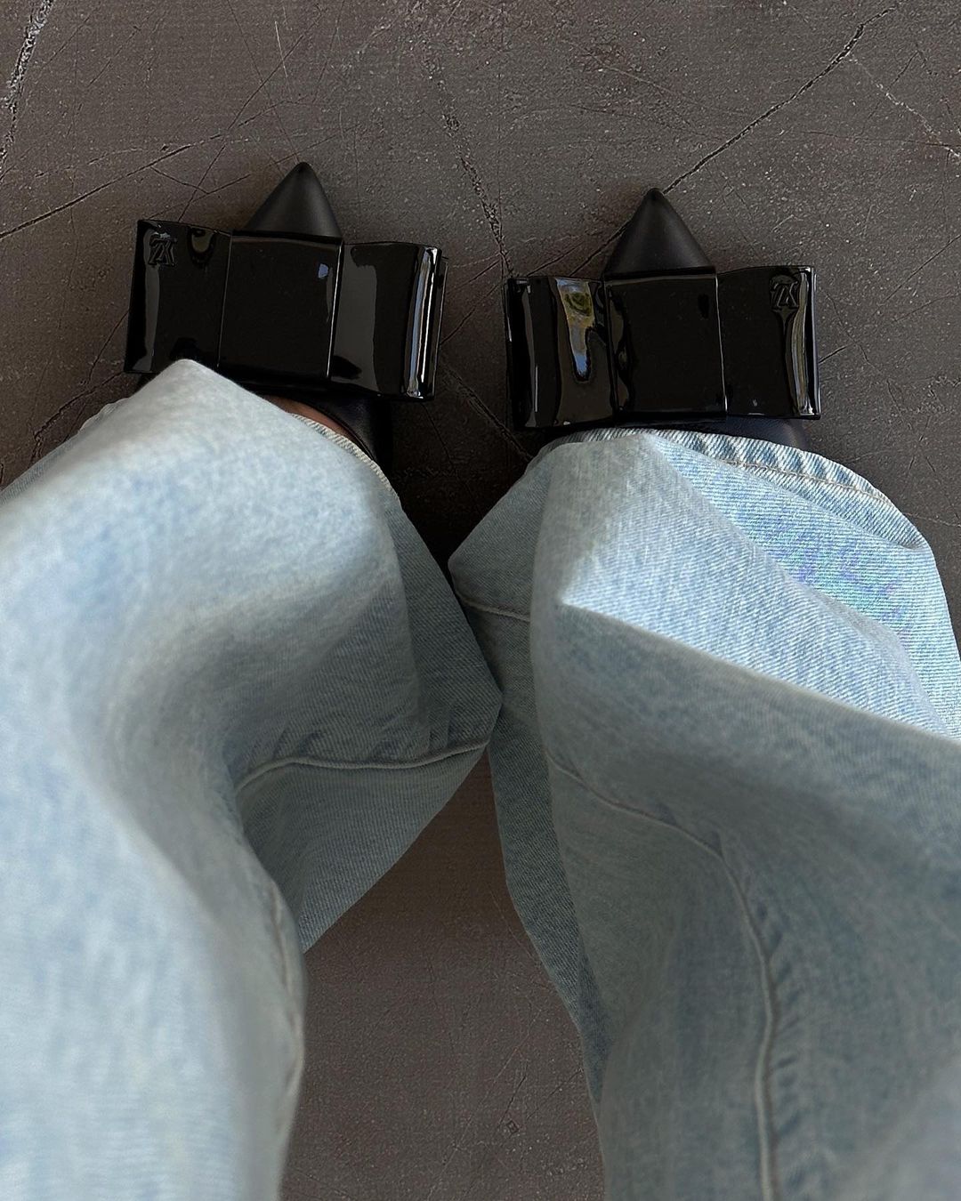 View of woman's legs and feet wearing light wash jeans and black high heel shoes on a neutral background, close-up shot.
