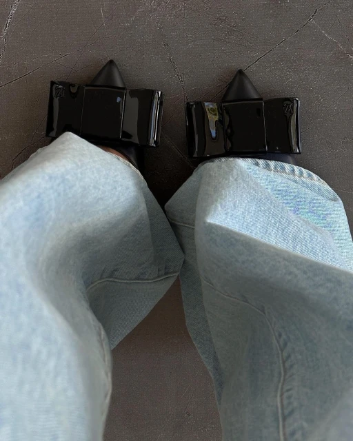 View of woman's legs and feet wearing light wash jeans and black high heel shoes on a neutral background, close-up shot.