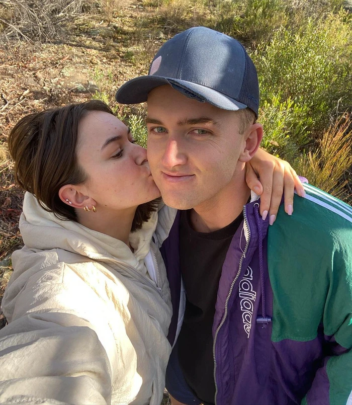 Young woman kissing a man on the cheek outdoors in a natural setting with foliage