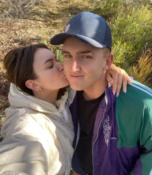 Young woman kissing a man on the cheek outdoors in a natural setting with foliage