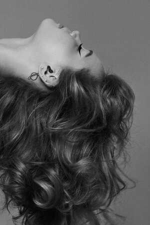 Close-up profile of a woman with voluminous textured curls and winged eyeliner against a grey backdrop