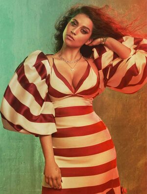 Brunette woman in a red and white striped dress with balloon sleeves poses against a mottled greenish-brown background in studio lighting.