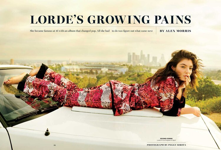 Singer Lorde lies on a white car hood, wearing patterned pants and top; city skyline in the distance; sunny day; outdoor setting.