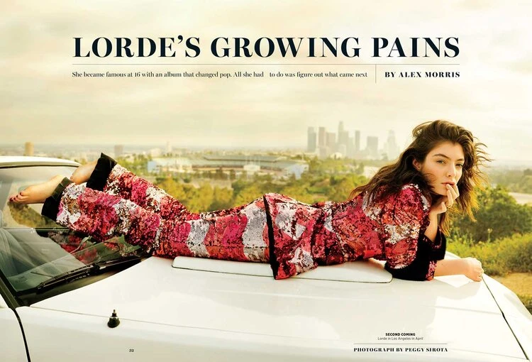 Singer Lorde lies on a white car hood, wearing patterned pants and top; city skyline in the distance; sunny day; outdoor setting.