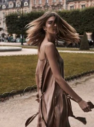 Woman in a glossy silk slip dress with long hair whipping in motion outdoors in a public square