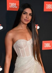 Priyanka Chopra wearing a white strapless corset dress with long dark hair against a branded step and repeat backdrop.