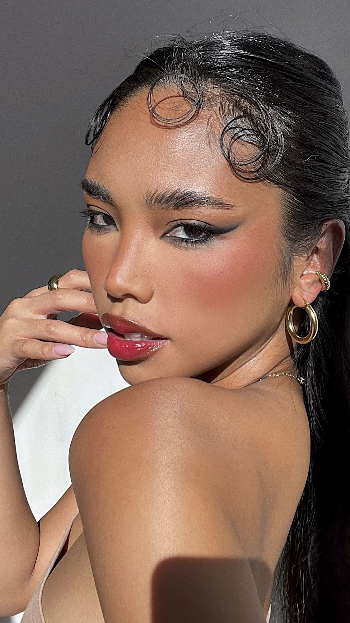 Close-up portrait of an adult woman with dark hair styled with finger waves, wearing gold hoop earrings and makeup.