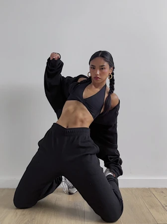 Woman kneeling in black athleisure wear with braided hair against a plain white wall