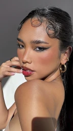 Close-up portrait of a woman with sleek dark hair, winged eyeliner, and glossy red lips wearing gold hoop earrings.