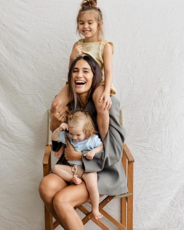 Smiling woman seated in a director's chair holding two children against a textured backdrop