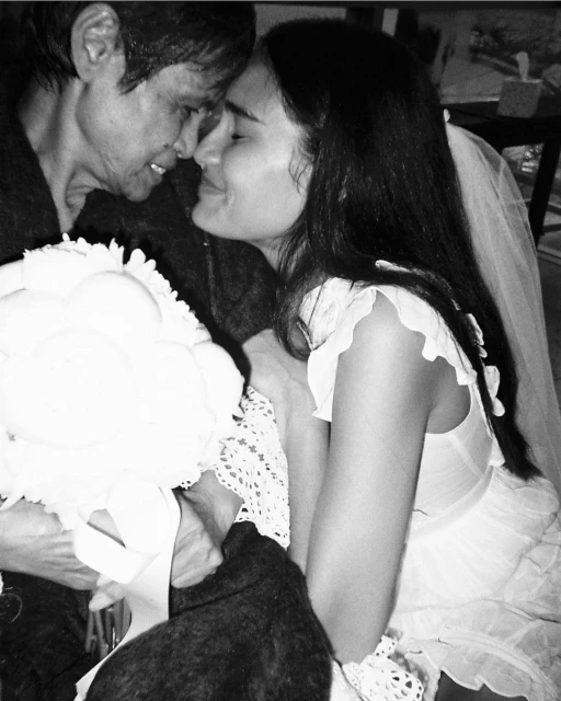 Close-up in black and white of a bride in a white dress and veil touching foreheads with an older adult female indoors.