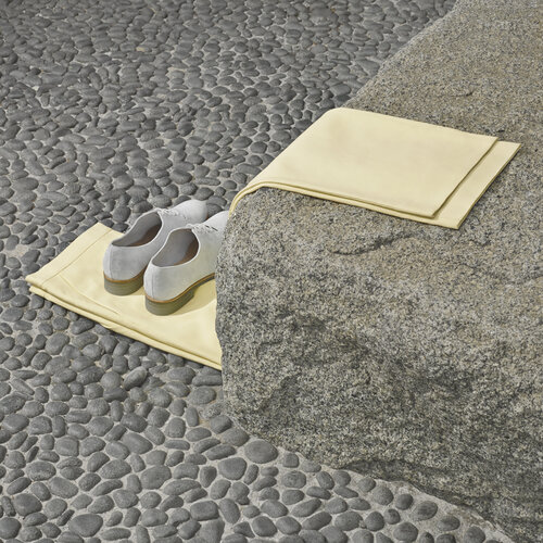 Still life of pair of grey leather shoes placed on a tan towel next to granite block. Grey pebble stone floor in background.