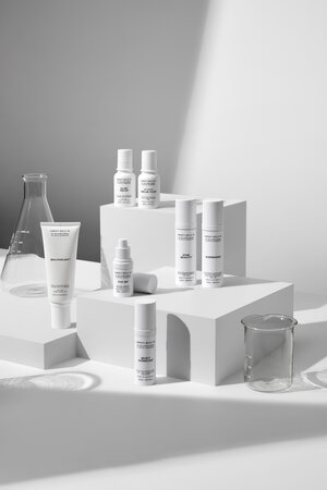 Minimalist product shot features an arrangement of skincare products on white geometric platforms, set against a clean, bright background.