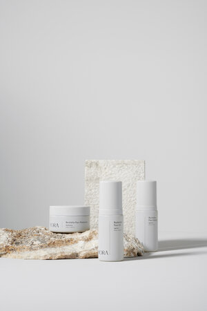 Still life shot of beauty products, including a cream jar and deodorant containers, displayed on a light rock surface against a white background.