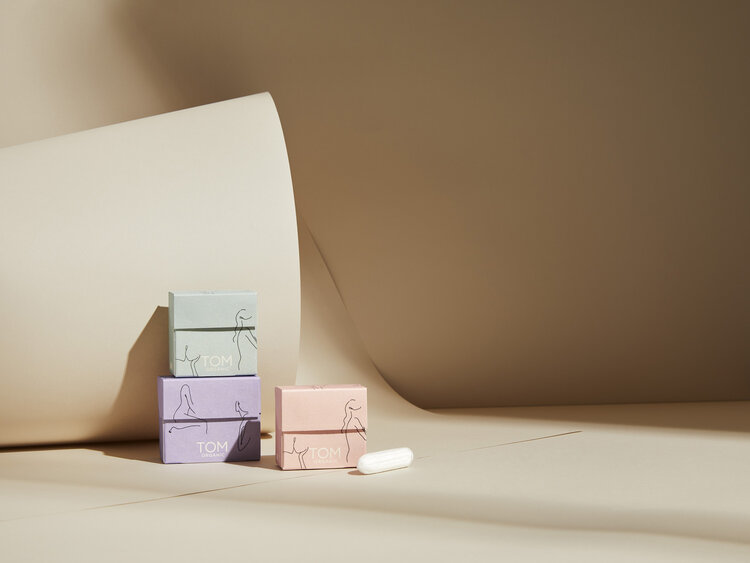 Product shot of three boxes stacked and a pill, featuring minimalist line art, set against a neutral-toned backdrop with soft, diffused light.