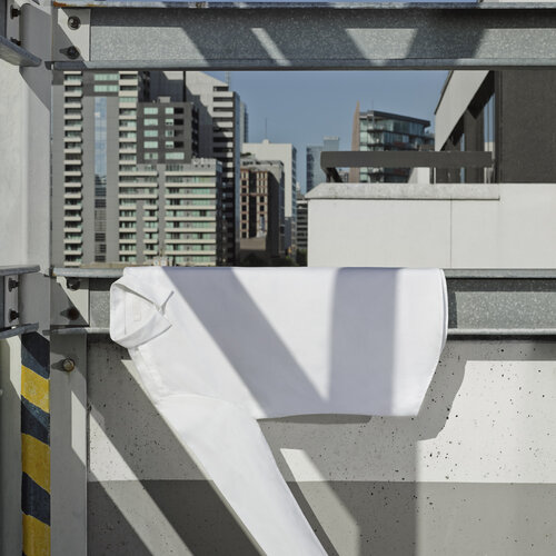 White shirt hanging inside a metal frame, with a high-rise city skyline visible in the background, under bright sunlight.