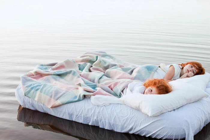 Two red-haired children lying on a white mattress floating in calm water styled by Rebecca Vitartas in Melbourne