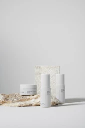 Three white skincare product containers resting on textured stone surfaces against a light grey background styled by Rebecca Vitartas