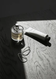 Round perfume bottle, white skincare tube and silver earrings arranged on dark textured wood surface