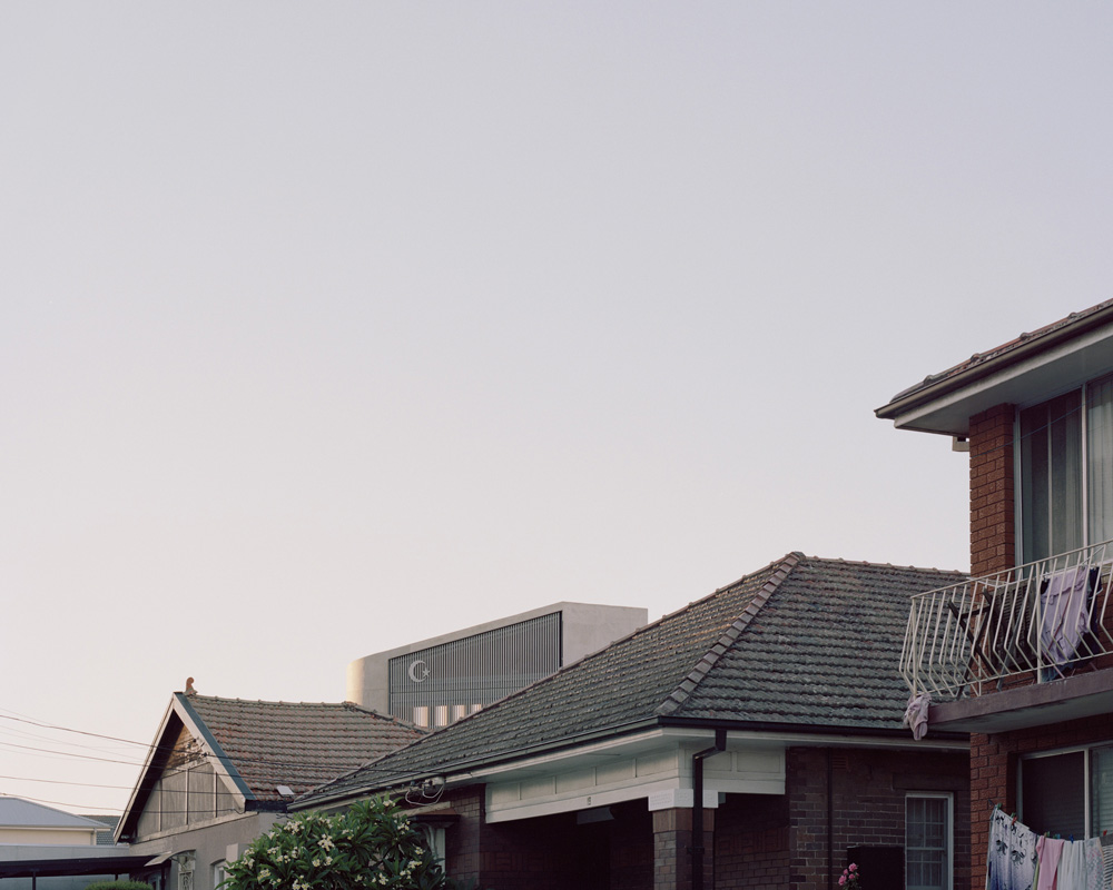 Exterior daytime shot of suburban houses with tiled roofs and brick walls, featuring residential architecture and clear sky above.