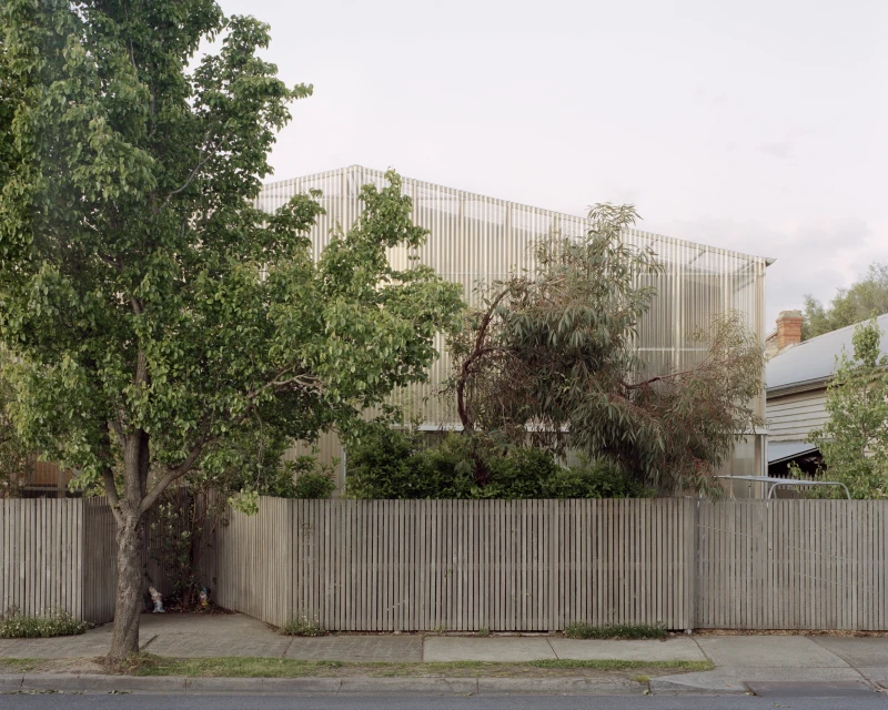 Exterior of modern house with vertical slat siding, complemented by surrounding trees and a wooden fence, creating a suburban atmosphere.