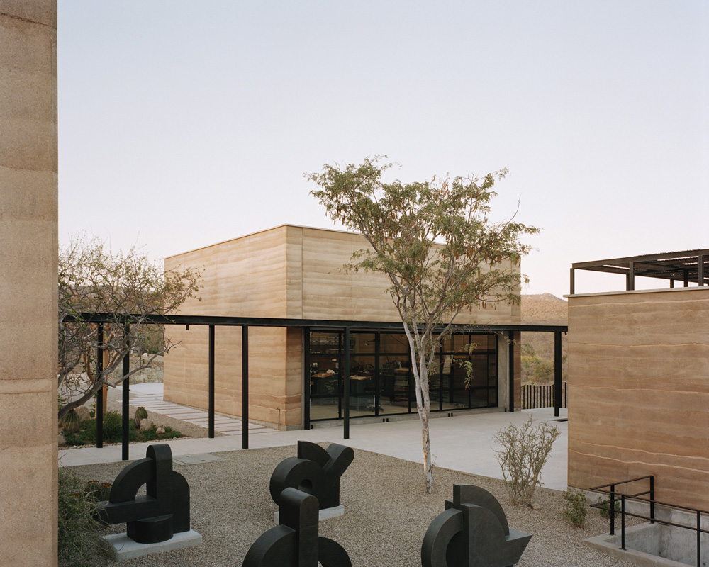 Exterior of a modern building featuring a minimalist design with light brown walls, black framed windows, and geometric art sculptures.