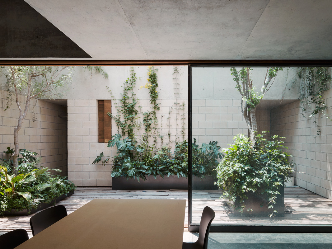Contemporary indoor-outdoor space with garden, seen through large glass doors; neutral palette, greenery, modern design, dining table, chairs.
