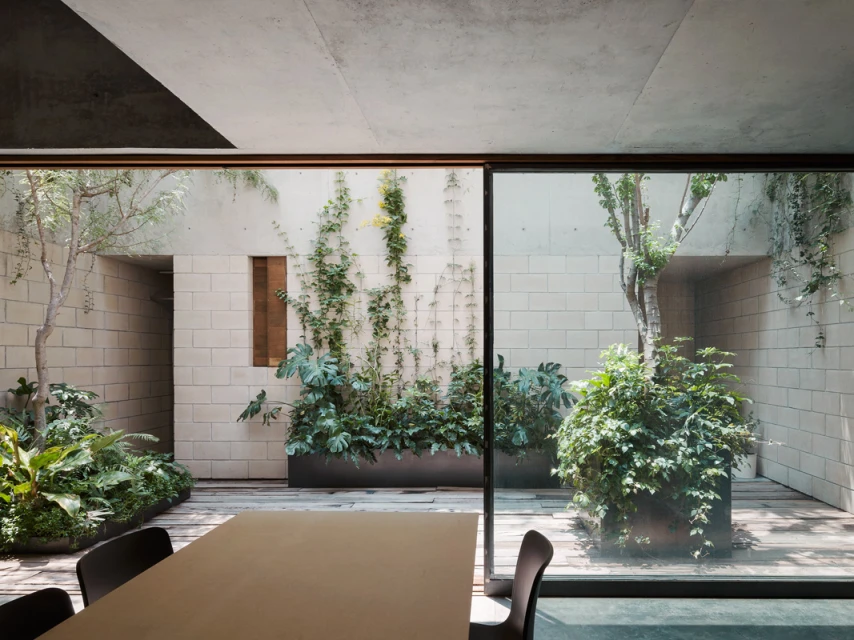 Contemporary indoor-outdoor space with garden, seen through large glass doors; neutral palette, greenery, modern design, dining table, chairs.