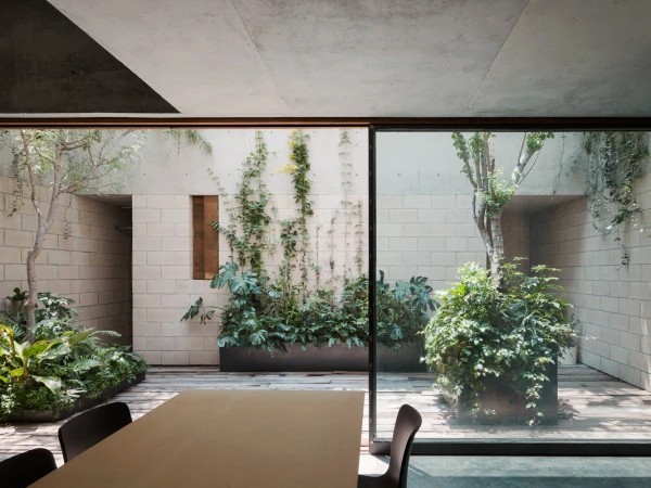 Contemporary indoor-outdoor space with garden, seen through large glass doors; neutral palette, greenery, modern design, dining table, chairs.