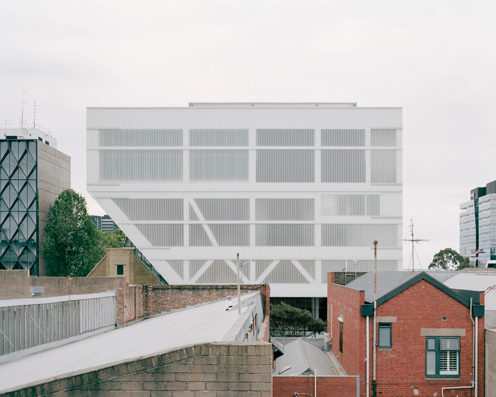 Modern white architectural building exterior viewed above surrounding urban rooftops and brick walls by Rory Gardiner