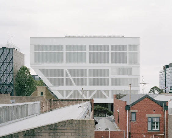 Modern white architectural building exterior viewed above surrounding urban rooftops and brick walls by Rory Gardiner