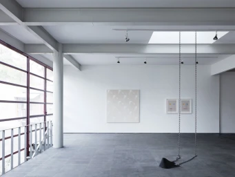 Minimalist art gallery interior with steel beams, large windows, and a suspended metal chain installation by Rory Gardiner