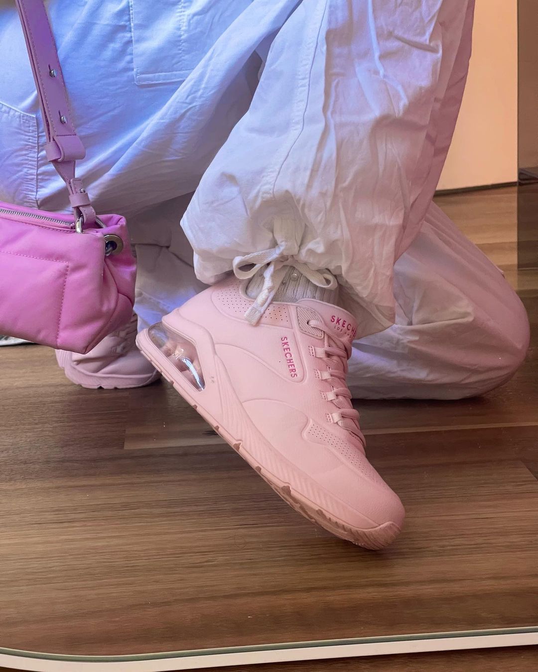 Pink Skechers sneakers and quilted pink bag, styled with white cargo pants on a hardwood floor reflecting in a low angled mirror.