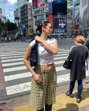 Woman in culottes stands on crosswalk in Shibuya, Japan, with buildings and billboards in the background, on a sunny day.