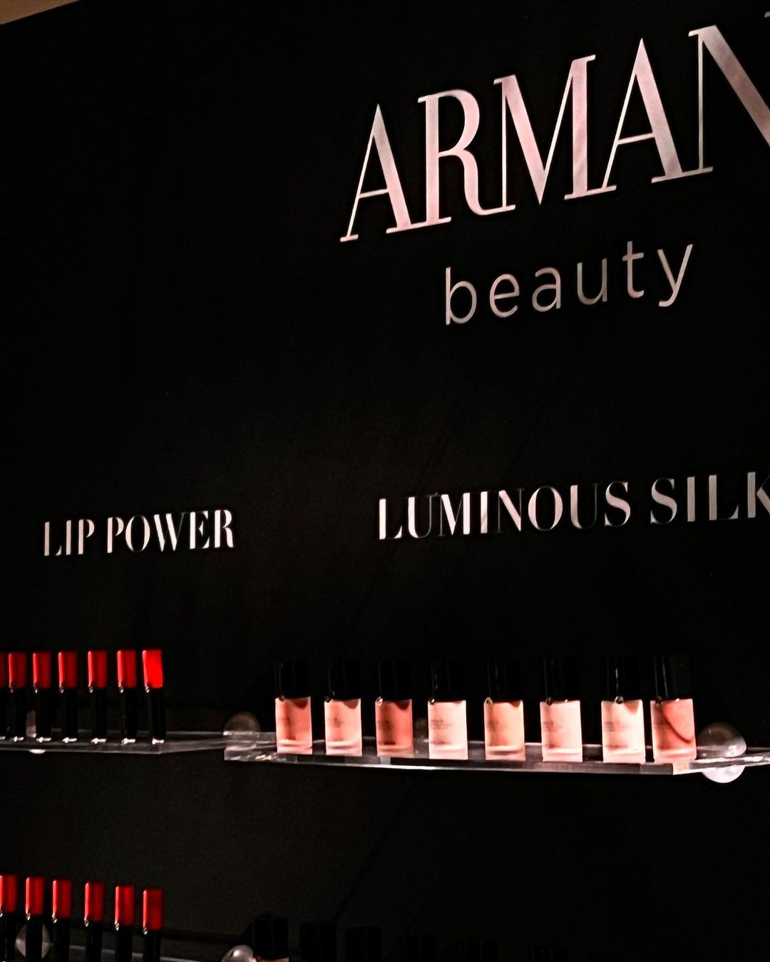 Armani Beauty display featuring rows of lipsticks and Luminous Silk products against a dark background with the brand logo.