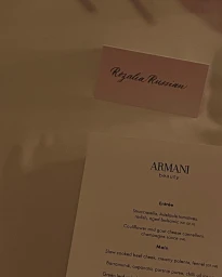 Close-up of an Armani Beauty event menu and a place card bearing the name Rozalia Russian on a white tablecloth.