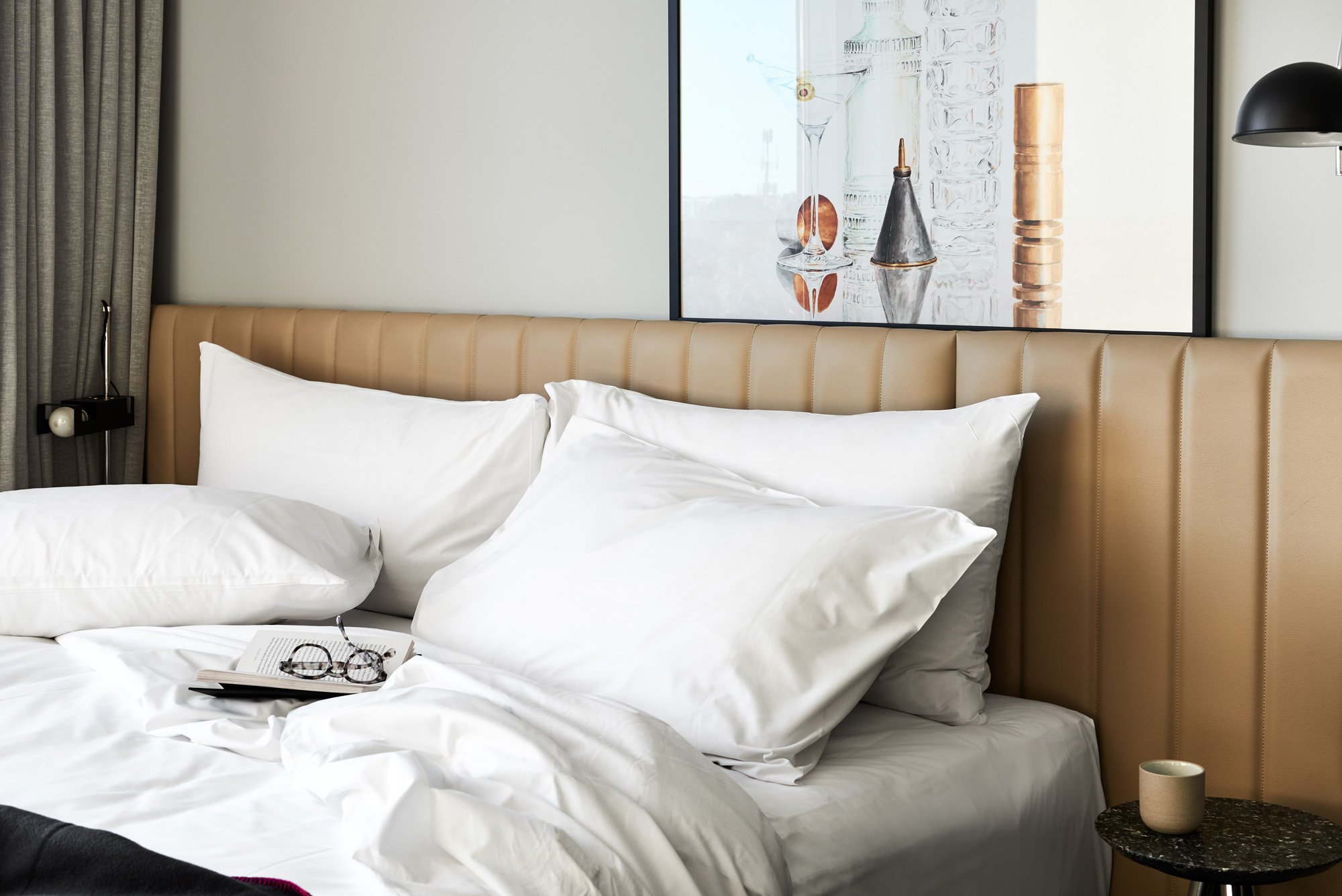 Bedroom scene featuring a made bed with white linens, pillows, and a tan headboard, complemented by a framed picture on the wall.