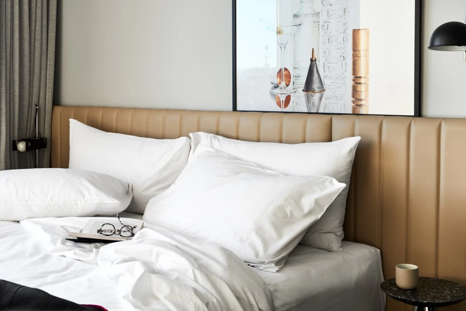 Bedroom scene featuring a made bed with white linens, pillows, and a tan headboard, complemented by a framed picture on the wall.