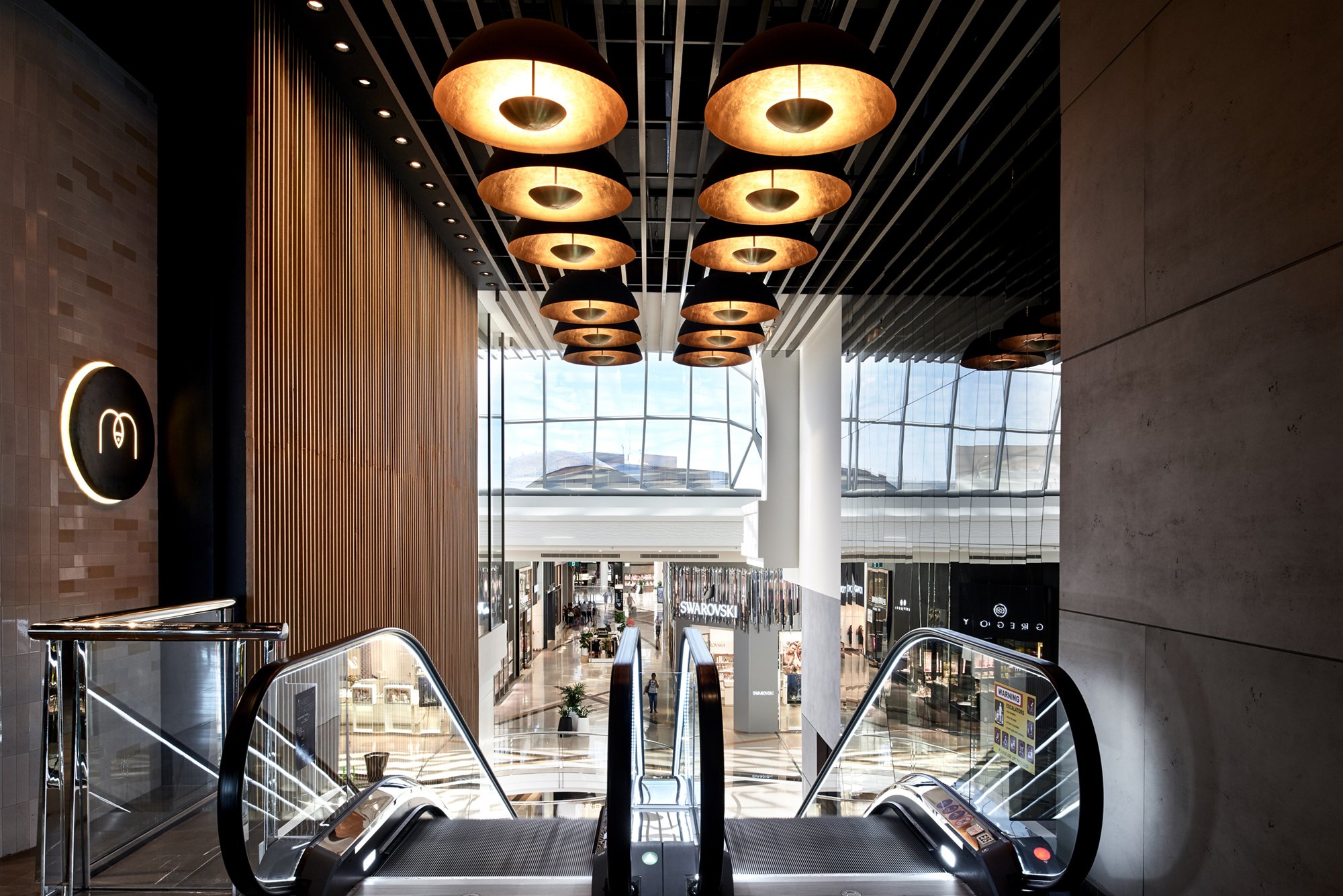 Interior view of modern commercial space featuring escalators, overhead lighting, and large windows in a shopping center.