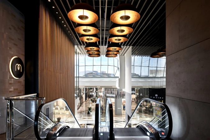 Interior view of modern commercial space featuring escalators, overhead lighting, and large windows in a shopping center.