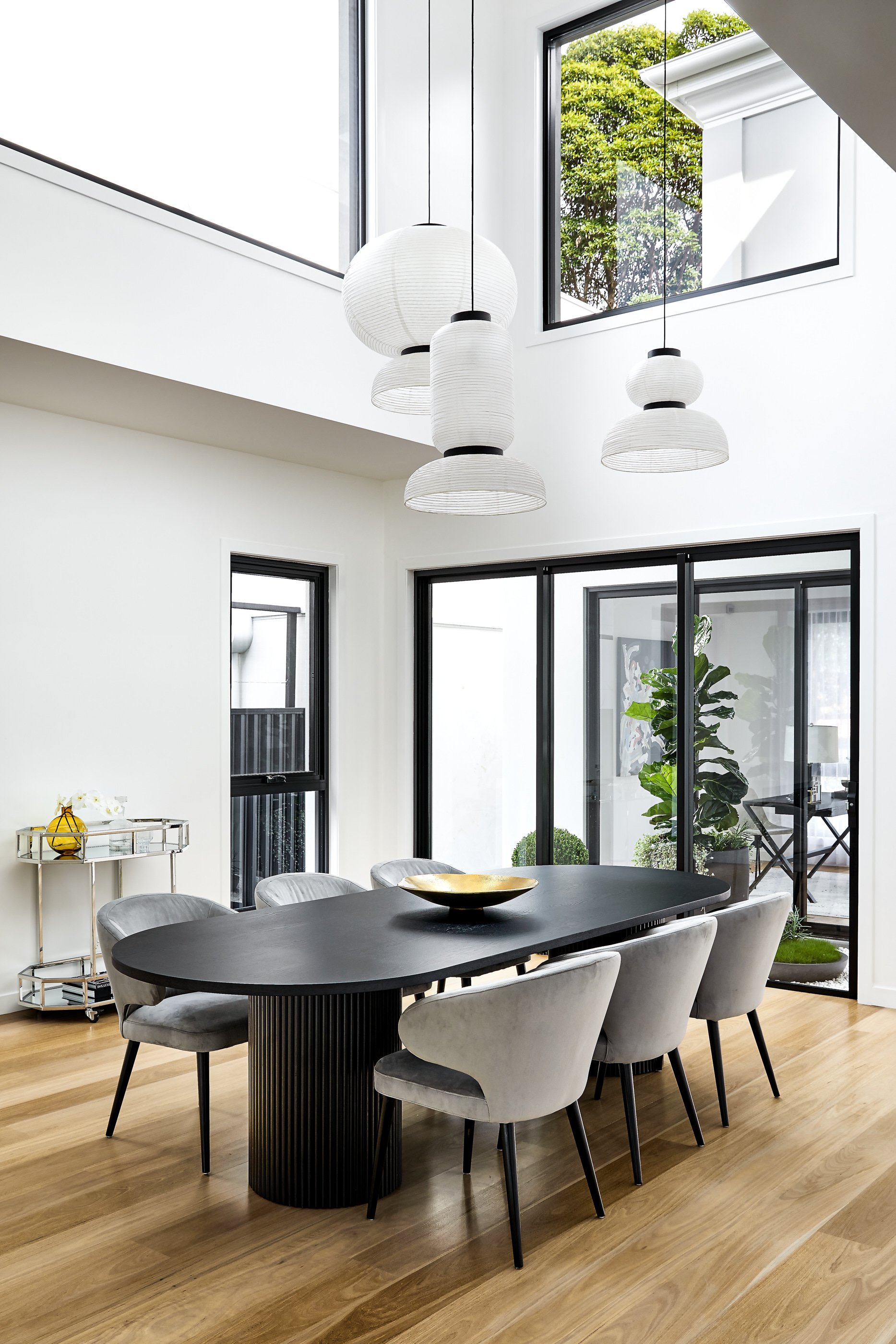 Contemporary dining room featuring a black oval table surrounded by gray chairs under unique white pendant lights, light wood flooring.